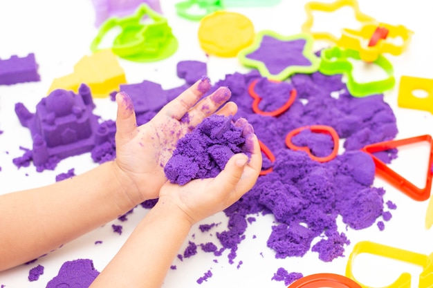 Childrens hands plays kinetic sand in quarantine. purple sand on a white table. coronavirus pandemic