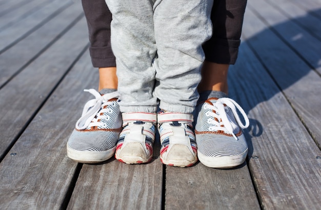 Фото Детские ножки и ступни в обуви, взрослые кроссовки друг с другом на деревянном фоне