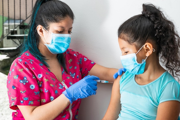사진 어린이 간호사가 갈색 소녀들에게 주사를 주사하여 집집 백신 접종 계획을 수립합니다.