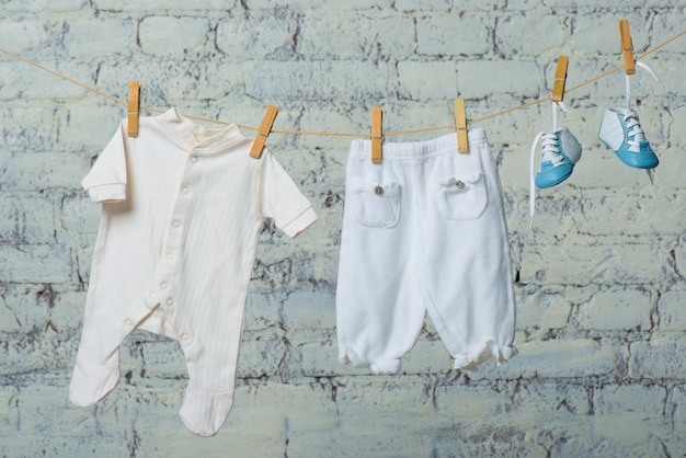 Childrens white body boots and pantyhose dry on a rope against a white brick wall