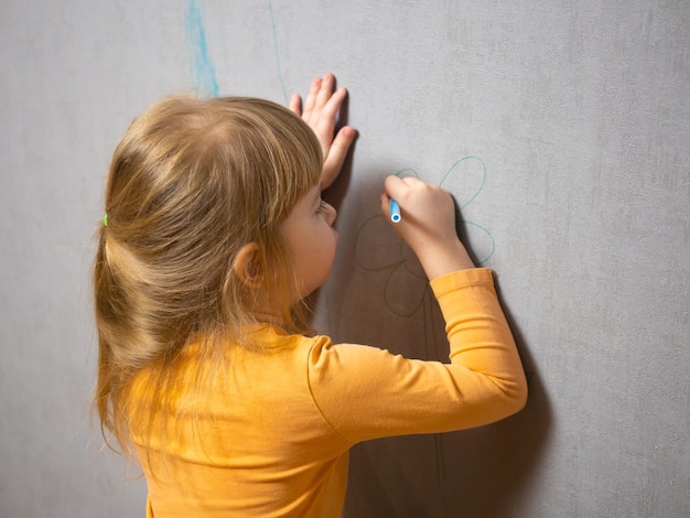 Foto lavoro per bambini una ragazzina disegna con una penna a punta di feltro sulla carta da parati a casa