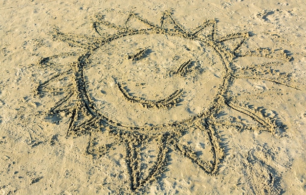 Childs drawing of smiling sun on yellow sand