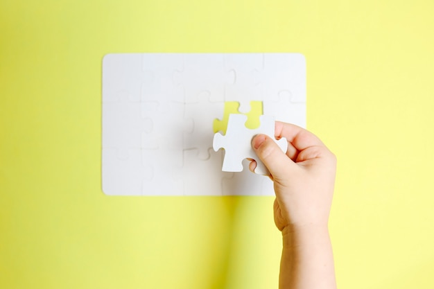 Photo childs hand holding the last piece of white puzzle on yellow table