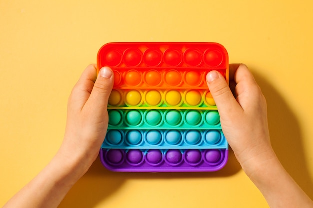 A childs hands presses on pop it toy silicone on yellow