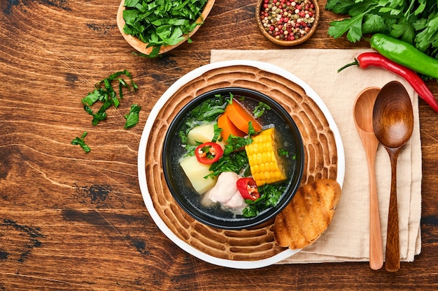 Chilean meat soup with pampkin, corn, fresh coriander and potatoes on old wooden table background. Cazuela. Latinamerican food.