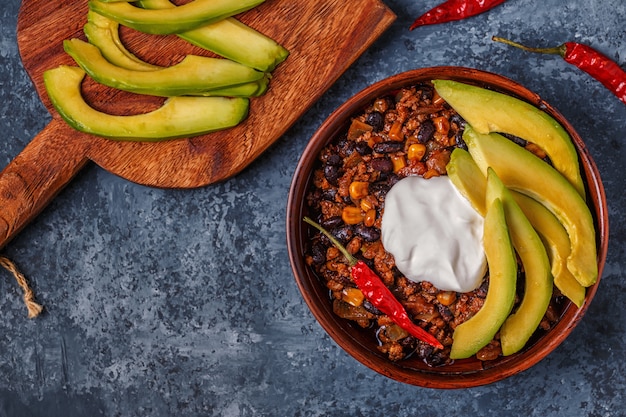 Chili con carne in bowl with avocado and sour cream.