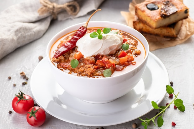 Chili con carne. Traditional recipe. Large portion of stew with beans, hot peppers, spices and fresh herbs. A large portion is served in a bowl with fresh sour cream.