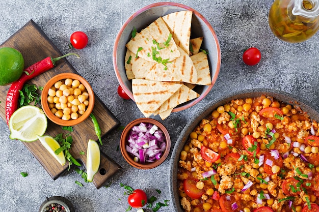 Chili con carne of turkey  with chickpeas served with nachos.  Chili with meat, nachos, lime, hot pepper. Mexican / Texas traditional food. Top view