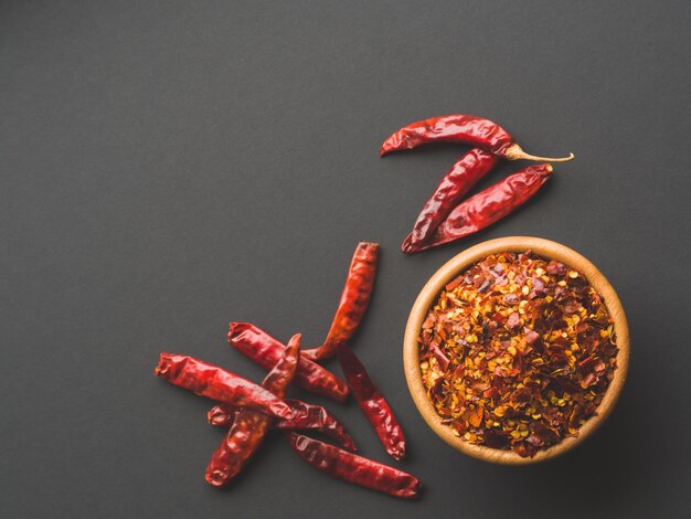 Foto fiocchi di peperoncino nella ciotola di legno e peperoncini secchi su sfondo di carta nera frutta secca e schiacciata