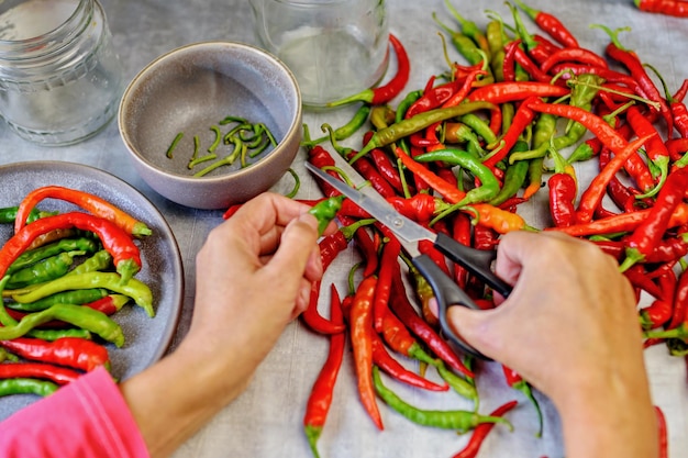 Foto chili peper. voorbereiding voor het inblikken van veelkleurige peulen van bittere peper. de groene punten afknippen met een schaar.