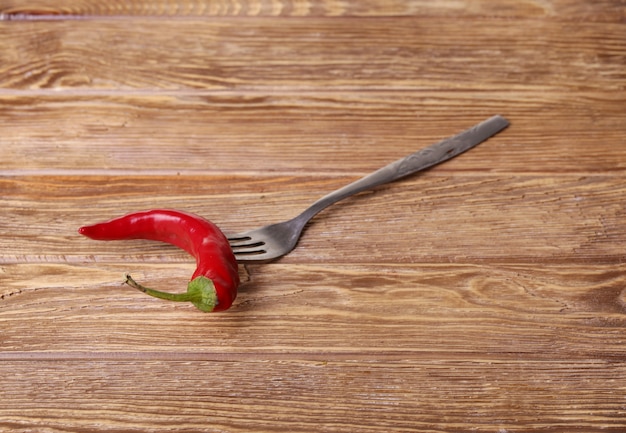 Chili pepper on fork on wooden background