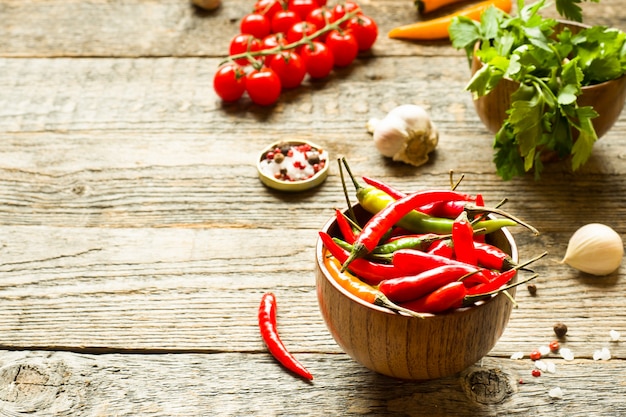 Chili pepper is spicy in a wooden bowl. Tomato parsley garlic on wooden rustic background