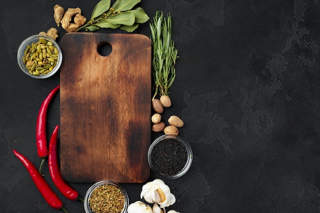 Chili peppers and spices with wooden board on black background