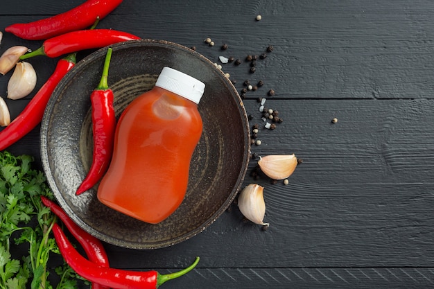 Chili sauce in bottle and peppers on dark wooden surface