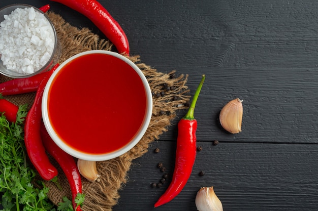 Chili sauce and peppers on dark wooden surface