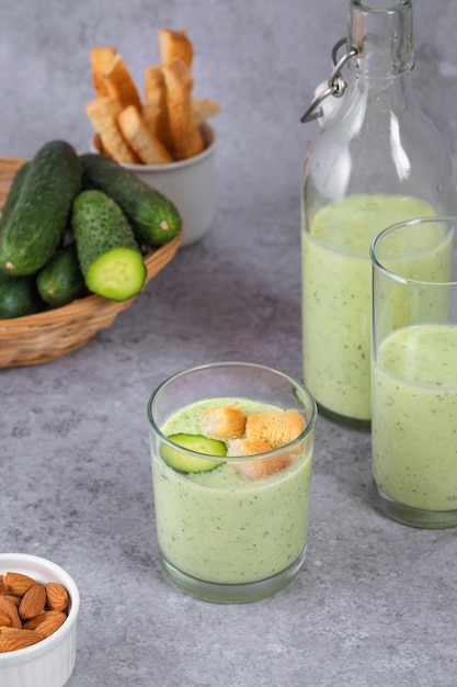 Chilled cucumber soup with nuts herbs yogurt crackers in a glass beaker on a gray background