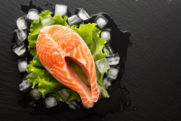 Chilled salmon steak in lettuce and ice on a stone background, top view, place for text