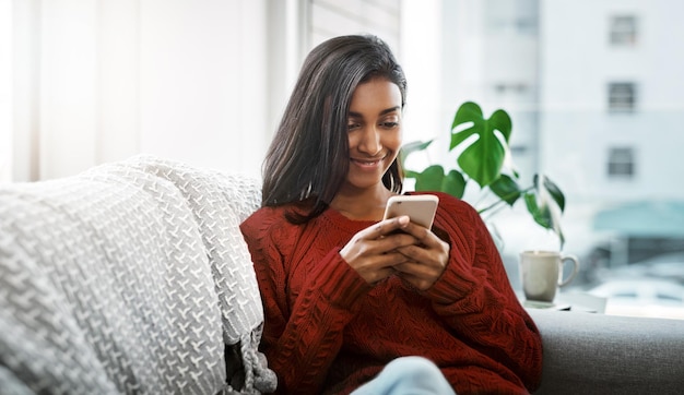 Chillen en chatten in de woonkamer Bijgesneden opname van een mooie jonge vrouw die een mobiele telefoon gebruikt terwijl ze thuis op de bank in de woonkamer aan het chillen is