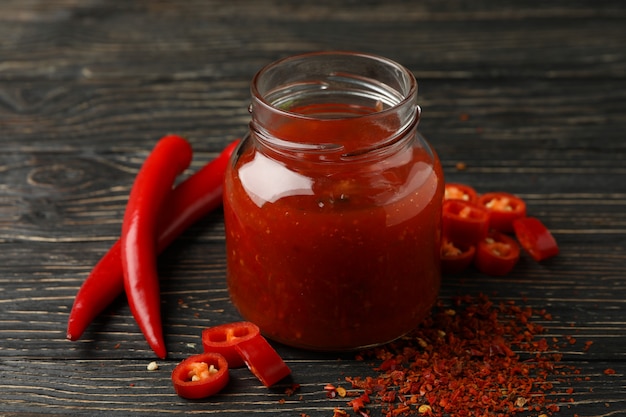 Chilli pepper and glass jar of sauce on wooden 