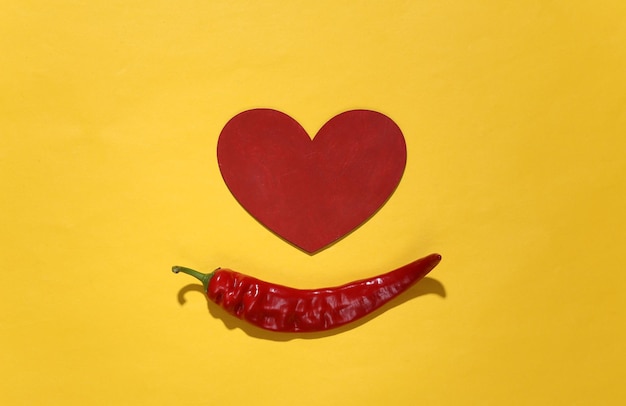 Photo chilli pepper and heart on a yellow background. love concept. top view