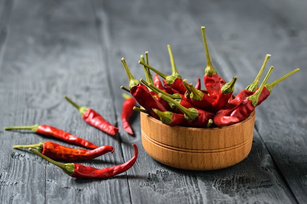 Chilli pods in a wooden bowl on a rustic black wooden table.