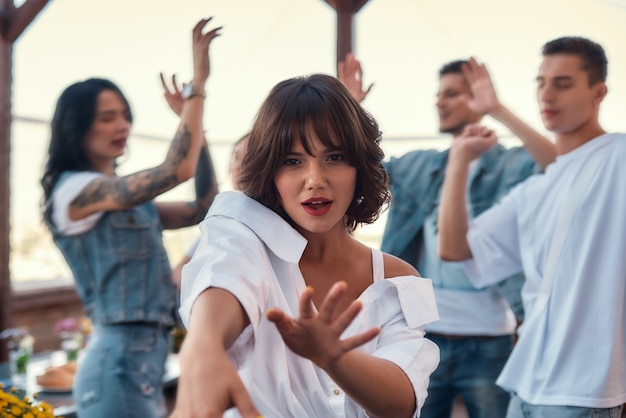 Chilling out pretty and young woman in white shirt is dancing and looking at camera