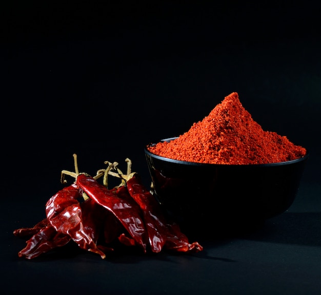 Chilly powder in black bowl with red chilly, dried chillies on black background