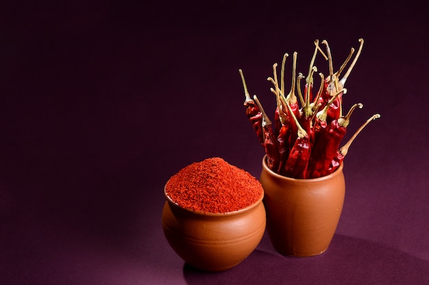 Chilly powder in clay pot with red chilly on wooden background