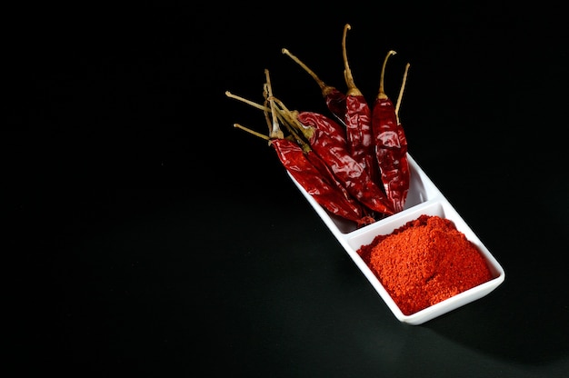 Chilly powder with red chilly in white plate, dried chillies on black surface