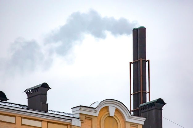 Photo chimney with smoke coming out of the heating stove on the roof of the building