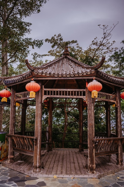 Lanterne rosse cinesi di viaggio della cina che appendono su una pagoda o su un gazebo di legno nel parco naturale per l'insegna lunare cinese di celebrazione del nuovo anno