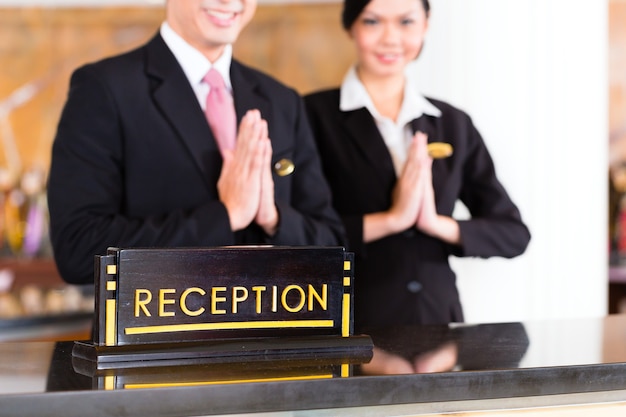 Chinees Aziatisch receptieteam bij de receptie van het luxe hotel verwelkomt gasten met typisch gebaar, een teken van goede service en gastvrijheid