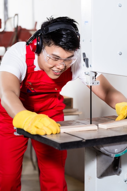 Chinese arbeider op zaag in industriële fabriek die een werkstuk snijdt