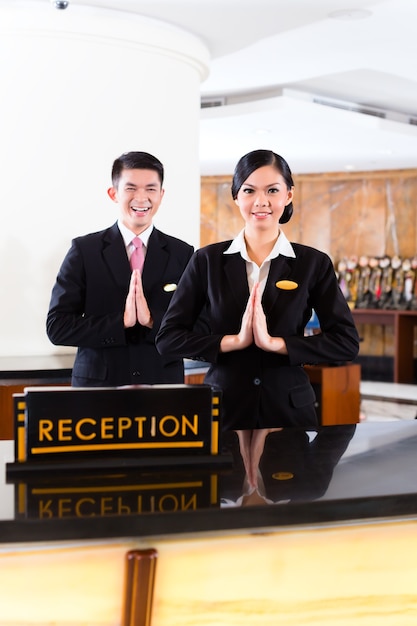 Chinese Asian reception team at luxury hotel front desk welcoming guests with typical gesture, a sign of good service and hospitality