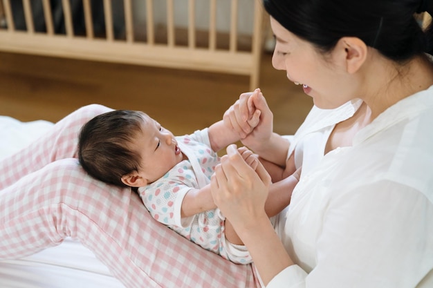 어머니의 다리에 누워있는 중국 아기는 순진해 보입니다. 귀여운 어린 유아의 높은 각도에서 그녀의 즐거운 미라와 상호 작용하고 있습니다.