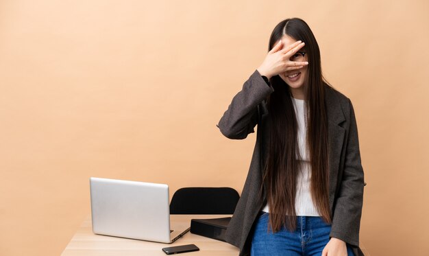 Chinese bedrijfsvrouw in haar werkplaats die ogen behandelen door handen en te glimlachen