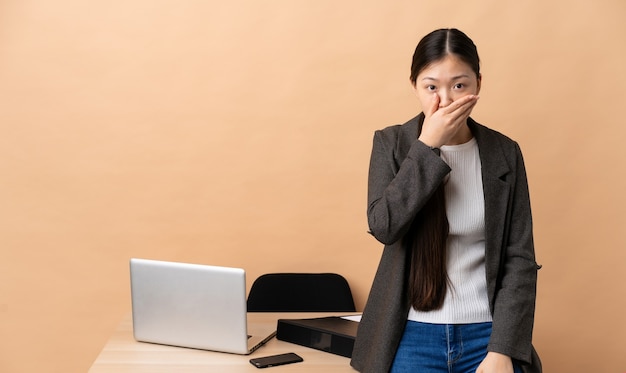 Chinese business woman in her workplace covering mouth with hand