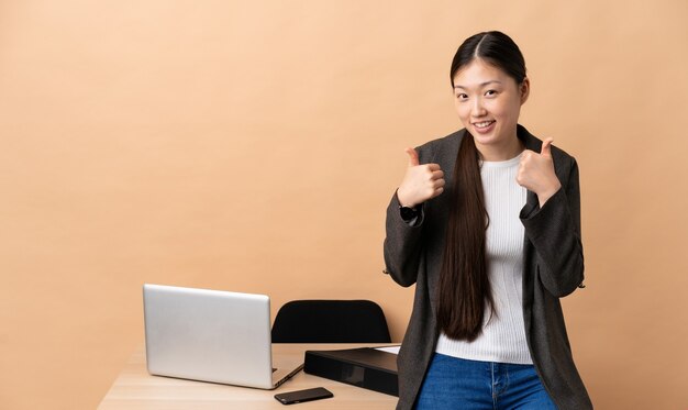 Chinese business woman in her workplace giving a thumbs up gesture