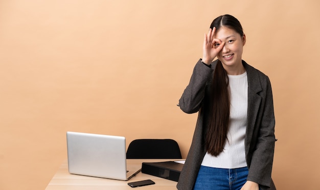 Китайская деловая женщина на своем рабочем месте, показывая пальцами знак ОК
