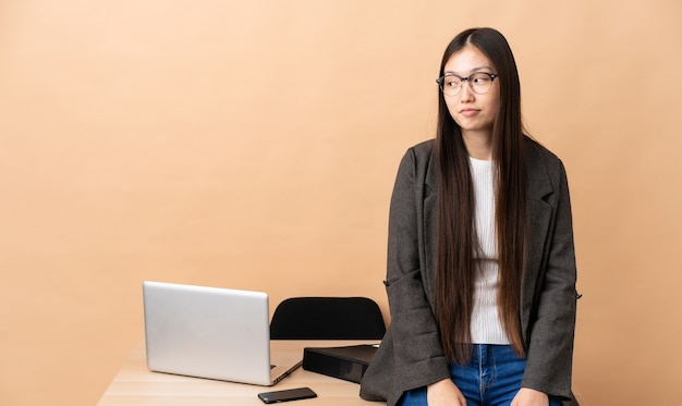 Китайская деловая женщина на своем рабочем месте, делая жест сомнения, глядя в сторону