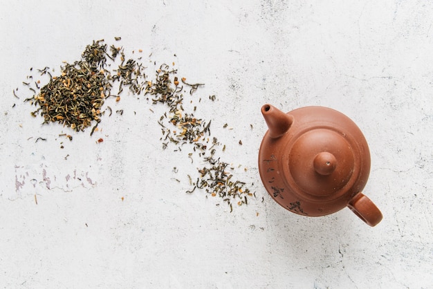 Chinese clay teapot with herbs on white concrete backdrop