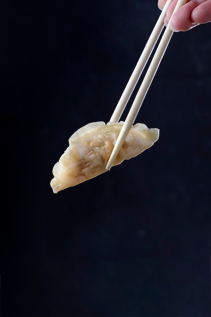 Chinese dumpling held up by chopsticks with black background