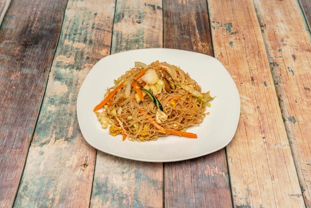 Chinese fine noodles stir fry with fresh vegetables and fried eggs on white plate