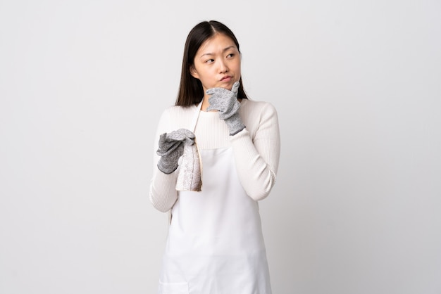 Chinese fishmonger wearing an apron and holding a raw fish on isolated white having doubts