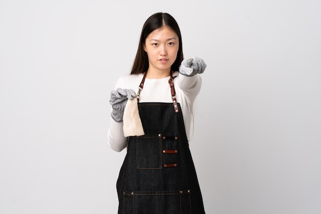 Chinese fishmonger wearing an apron and holding a raw fish over white wall frustrated and pointing to the front