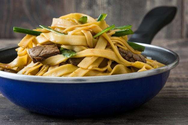 Chinese food beef chow mein in frying pan on wooden table on wooden table