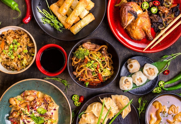 中華料理の暗い背景。中華麺、米、餃子、北京ダック、点心、春巻き
