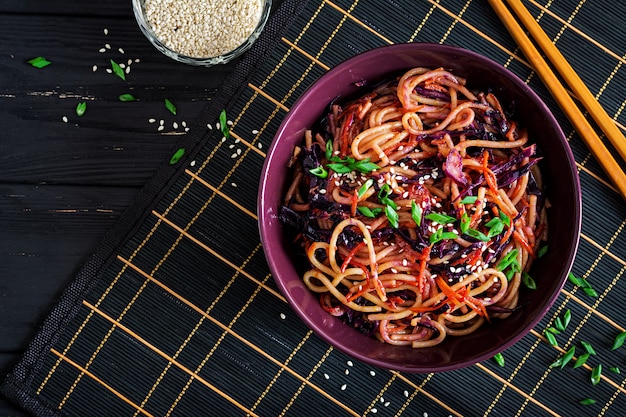 Chinese food. Vegan stir fry noodles with red cabbage and carrot in a bowl on a black wooden background. 