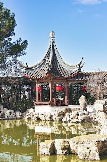 Gazebo cinese in giardino con lanterne tradizionali rosse cinesi sulla riva dello stagno sacrale delle carpe