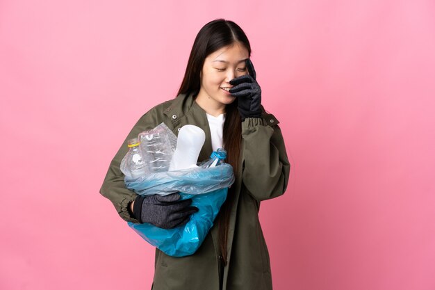 Chinese girl holding a bag full of plastic bottles to recycle on isolated pink laughing